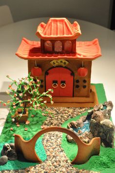 a small house made out of clay with rocks and trees in front of it on a white surface