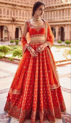 a woman in an orange lehenga standing on the ground with her hand on her hip