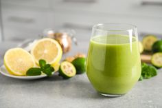 a glass filled with green liquid next to sliced lemons