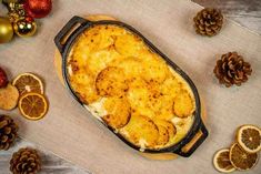 a casserole dish with oranges and pine cones around it on a table