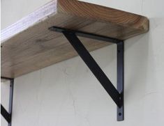 a wooden shelf with black metal brackets on it's sides and a white wall in the background