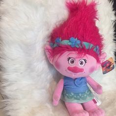 a pink troll doll sitting on top of a fluffy white rug with a tag in it's ear