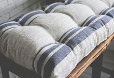 a wooden bench with blue and white striped cushions on it's seat cushion, in front of a brick wall