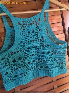 a blue crocheted top is hanging on a wooden hanger and it has holes in the back