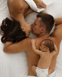 a man and woman laying in bed with a baby on their back, top view