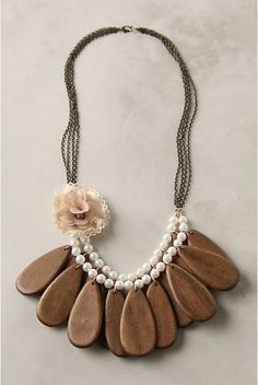 a brown and white necklace with flowers on the front, pearls hanging from it's sides