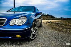 the front end of a blue car parked in a parking lot next to a hill