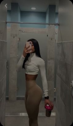 a woman is taking a selfie in the bathroom while holding a cup and looking at her cell phone