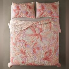 a bed with pink and white comforters on top of it next to a wall