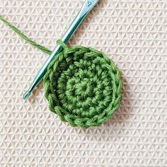 a green crochet ball sitting on top of a table next to a knitting needle