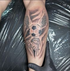 a person with a tattoo on their leg holding a soccer ball and wings above them