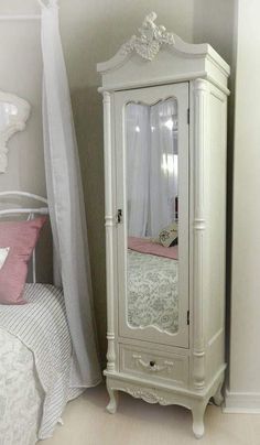 a white armoire next to a bed in a room with a pink pillow on it