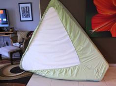 a green and white triangle shaped pillow sitting on the floor in front of a television