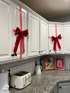 a kitchen with white cabinets and red bows on the backsplash, along with a toaster