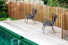 two chairs sitting on top of a wooden deck next to a pool