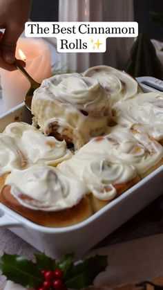 a person holding a spoon in a dish filled with cinnamon rolls and cream cheese frosting