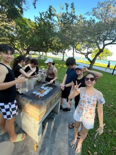 several people standing around a barbecue grill in the grass with one person giving the peace sign