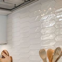 kitchen utensils and wooden spoons are sitting on the counter in front of a white tile backsplash