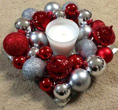 a candle sits in the center of a wreath made out of silver and red ornaments