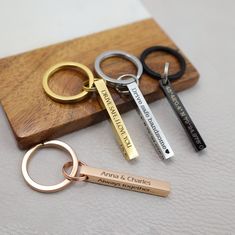 three personalized keychains are sitting on a wooden board with two different types of keys