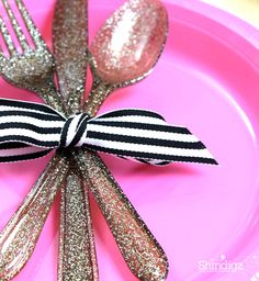 there is a pink plate with silver and black utensils wrapped in ribbon on it