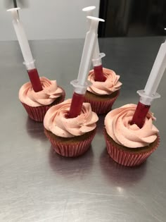 four cupcakes with pink frosting and two white candles sticking out of them