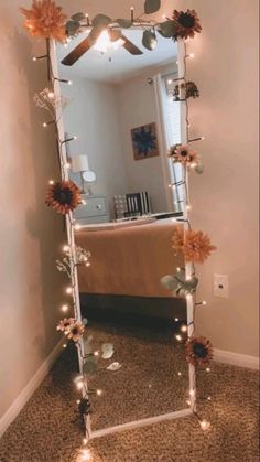 a mirror that has flowers on it and lights in front of it, reflecting the room