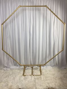 a gold hexagonal frame sitting on top of a white fur covered floor next to a curtain