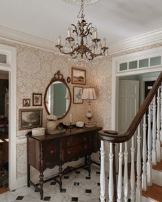 a room with a chandelier, table and mirror on the wall next to stairs