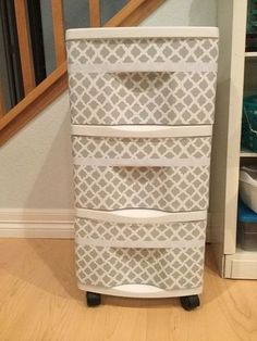 a white and grey dresser with drawers on wheels in front of a stair case next to a staircase