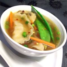 a white bowl filled with dumplings and veggies on top of a table