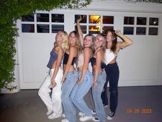 four girls posing in front of a garage with their arms up and one girl holding her head