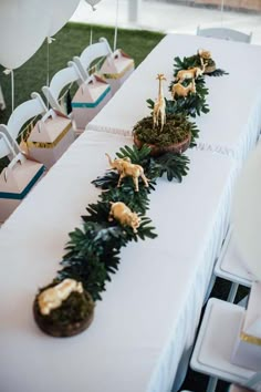 the table is set up for an event with white chairs and tables covered in greenery