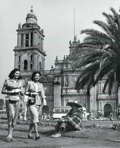 black and white photograph of two women walking in front of an old building with palm trees