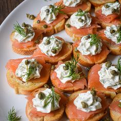 a white plate topped with crackers covered in cream cheese and smoked salmon slices, garnished with dill