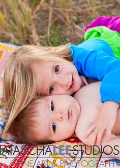 two young children laying on top of each other in front of a quilted blanket