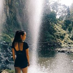 a woman standing in front of a waterfall with her back turned to the camera,