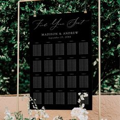 a black and white wedding seating chart on a gold frame with flowers in the foreground