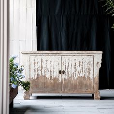 an old wooden cabinet sitting in front of a black curtain and potted plant next to it