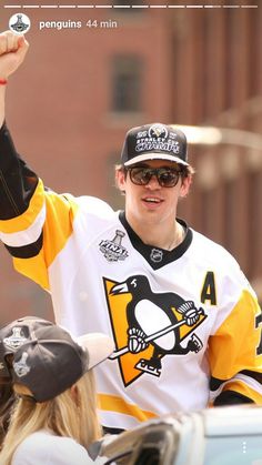 a man in a penguins jersey waves to fans from the back of a car on a city street