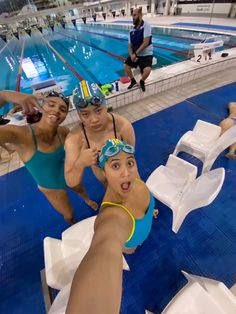 three women in swimsuits and goggles are taking a selfie at an indoor swimming pool