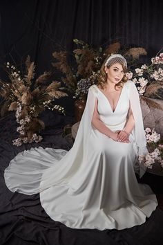 a woman in a white wedding dress sitting on a bed with flowers and foliage behind her