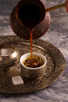 a person pours coffee into a small cup on a plate with ice cubes