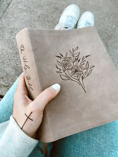 a person holding a brown book with flowers on it and writing on the front cover