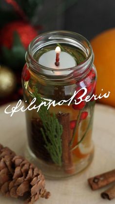 a candle is sitting in a jar with pine cones and cinnamons next to it