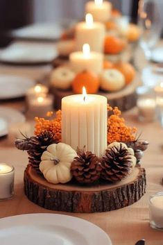 a table set with candles, pine cones and white pumpkins on top of it