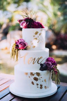 a three tiered wedding cake with purple flowers on top and the word love painted on it