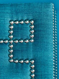 the letter h is made out of beads on a blue cloth with white stitching