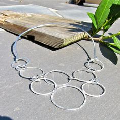 This Hammered Argentium Silver Organic Circles on a neck ring is another version of my silver triangle necklace. On this version, eight circles creating a V at the neckline, attach to a sterling neck ring with hooks at the end. I am really into this hook neck ring as a way to have a versatile, precious metal holder for several focal pieces. This is a comfortable, easy to close, way to make a style statement. The entire piece is handmade by me from Argentium Silver which is recycled silver.. The Diy Wire Earrings, Metal Jewelry Making, Neck Ring, Hammered Bangles, Gold Bangle Set, Triangle Necklace, Silver Bead Necklace, Swarovski Crystal Necklace, Wire Work Jewelry