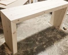 a wooden bench sitting on top of a cement floor next to a pile of wood